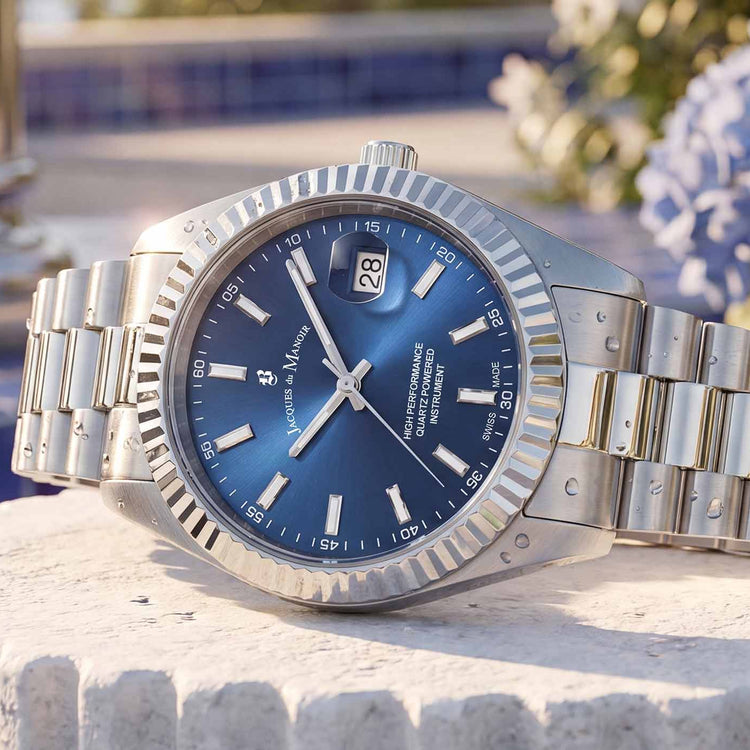 A Rolex Oyster Perpetual watch with a blue dial and silver metal bracelet, displayed on a stone pedestal with blue hydrangeas in the background.