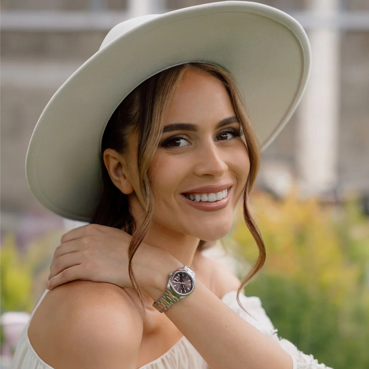 Woman wearing a white hat and white top with a blurred outdoor background