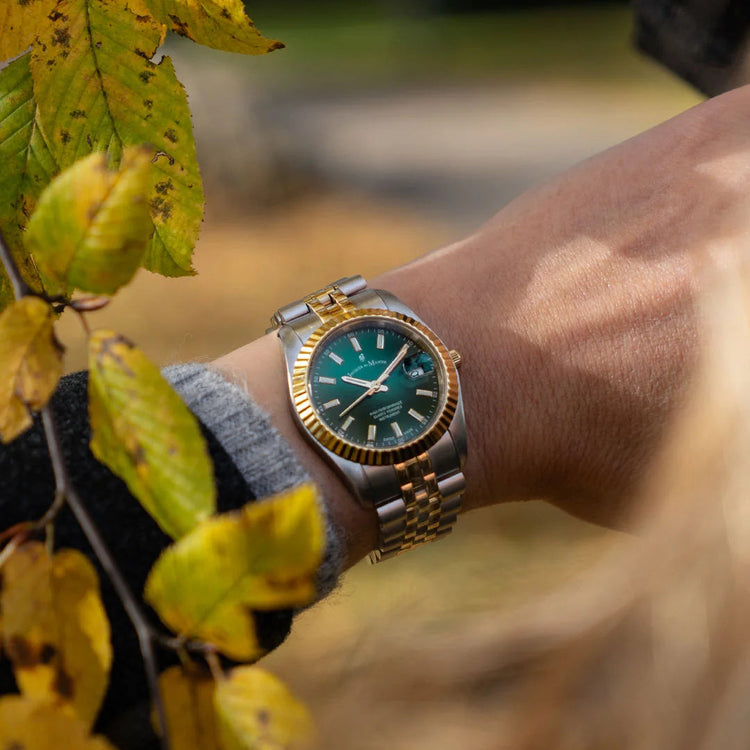 Gold and green watch on a wrist with autumn leaves in the background