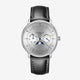 Sternglas Astronom watch with a silver dial, blue hands, moon phase indicator, and a black leather strap with white stitching, shown on a light gray background.