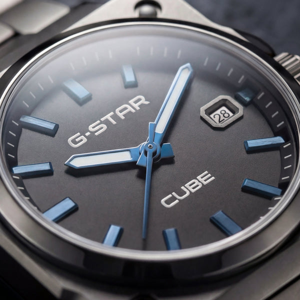 Close-up of a G-Star Cube watch with a dark gray dial, blue hands and markers, and a black metal case and bracelet.