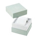 A white cylindrical watch or accessory roll displayed inside an open square presentation box with a pale mint green lid resting above it on a white background.