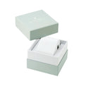 A white cylindrical watch or accessory roll displayed inside an open square presentation box with a pale mint green lid resting above it on a white background.