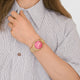 Person wearing a gold watch with a pink face on a white background