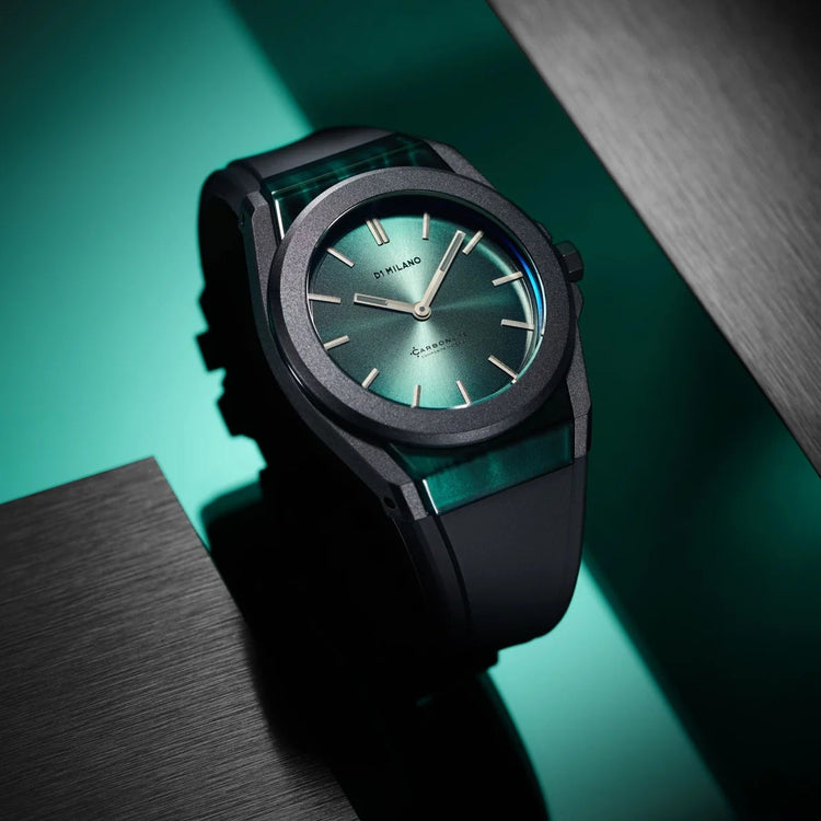 A sleek wristwatch with a dark gray case, a green dial, and a green translucent strap, resting on a dark teal and black background with brushed metal panels.