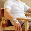 Person wearing a white shirt and watch sitting on a wooden chair.