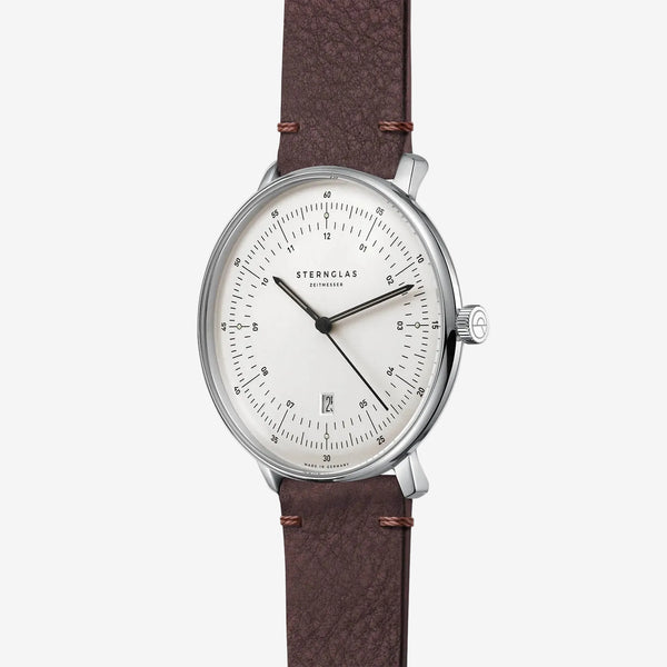 Sternglas by Swatch watch featuring a silver stainless steel case, a clean white dial with black hands and markers, and a textured brown leather strap with visible stitching.